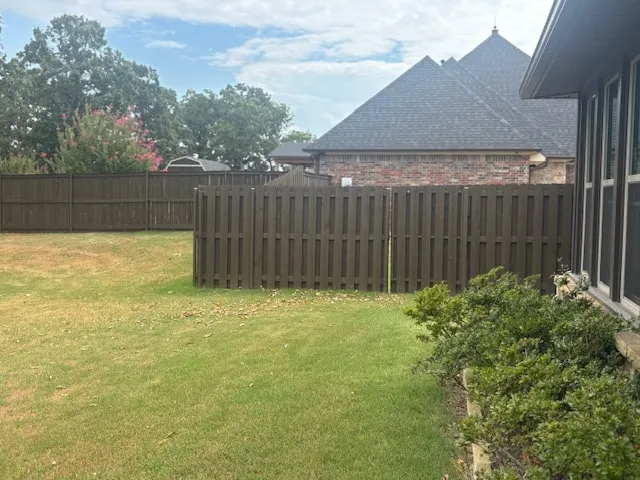 Backyard with a dark stained wood privacy fence beside a brick house with a gray shingle roof