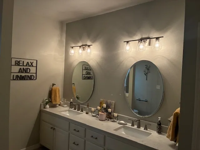 Bathroom with gray walls, a white double vanity and 2 round mirrors under black light fixtures