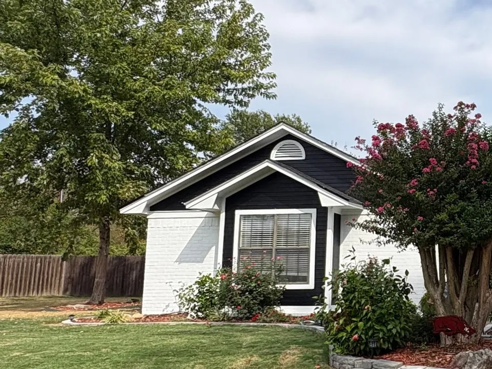 The same Fort Smith house seen from the street: black siding and white brick behind a crepe myrtle