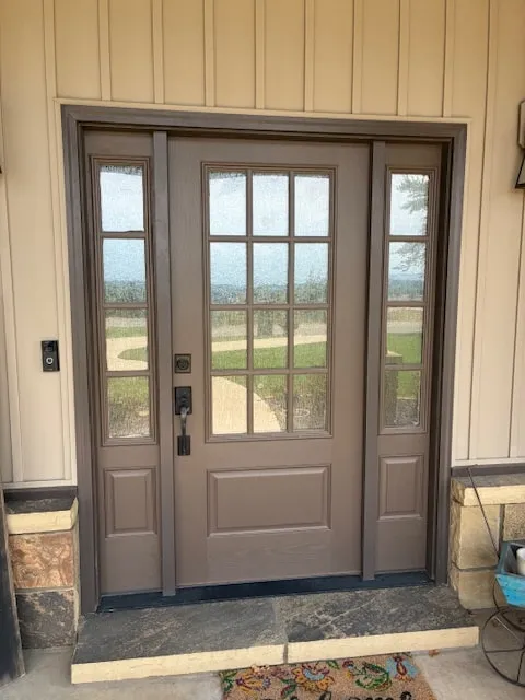 Front door painted a warm brown with glass sidelights, board and batten siding around it