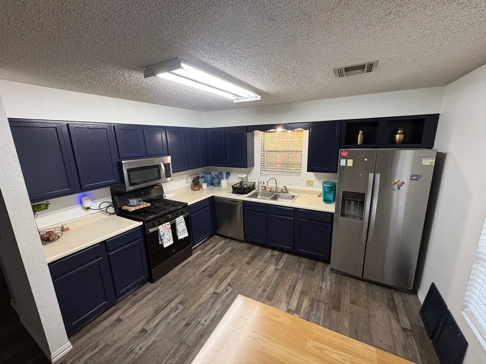 A kitchen after painting: Naval Blue cabinets above and below cream counters, a black range, a stainless refrigerator and a wood plank floor