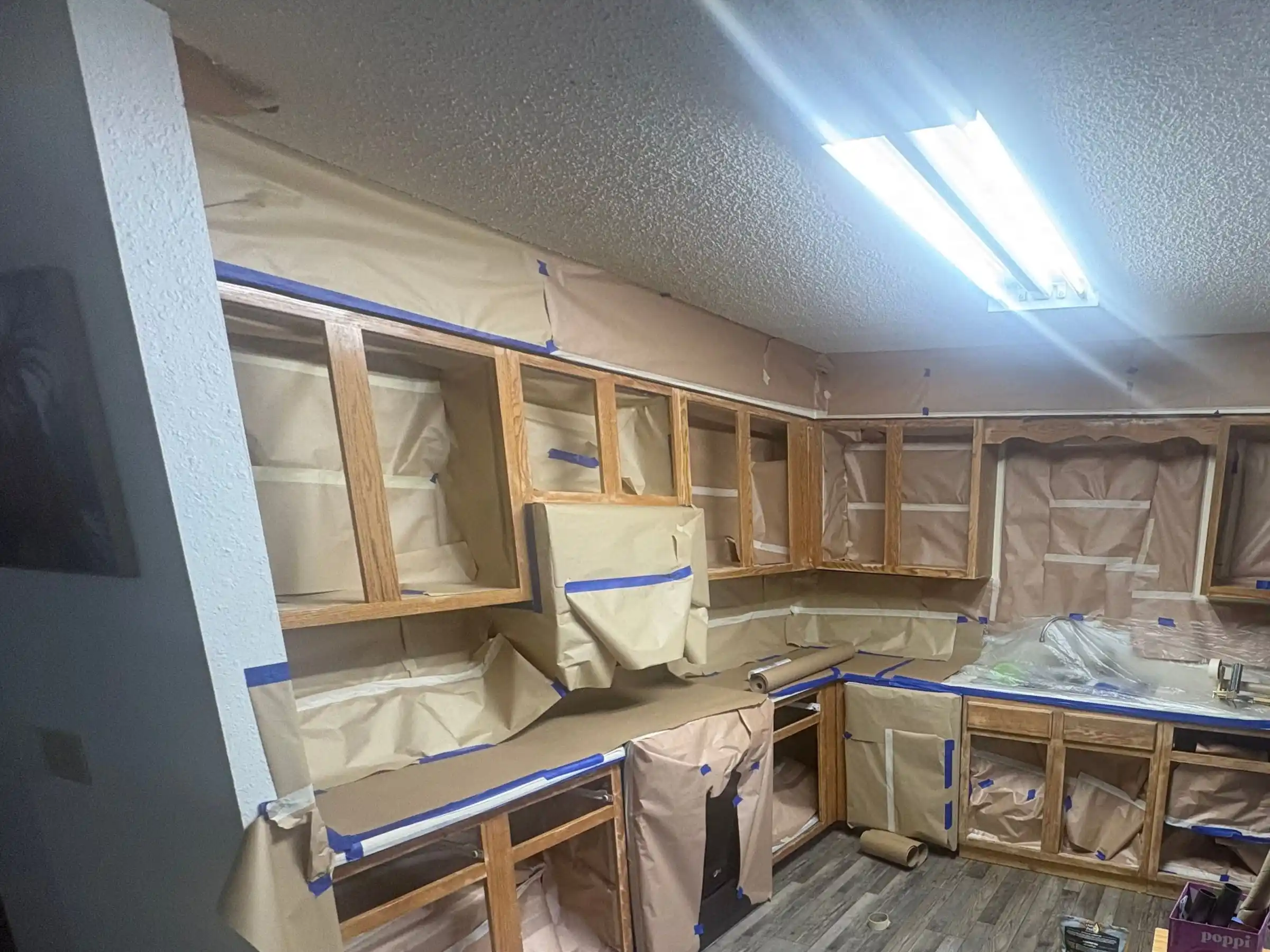 The same kitchen during the job: the doors off, the cabinet boxes sanded and the counters and walls covered in paper