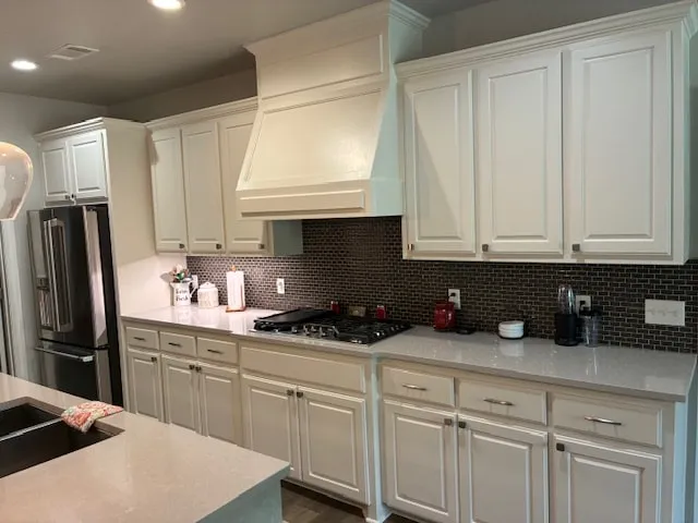 Kitchen with white painted cabinets, a dark tile backsplash and a stainless refrigerator