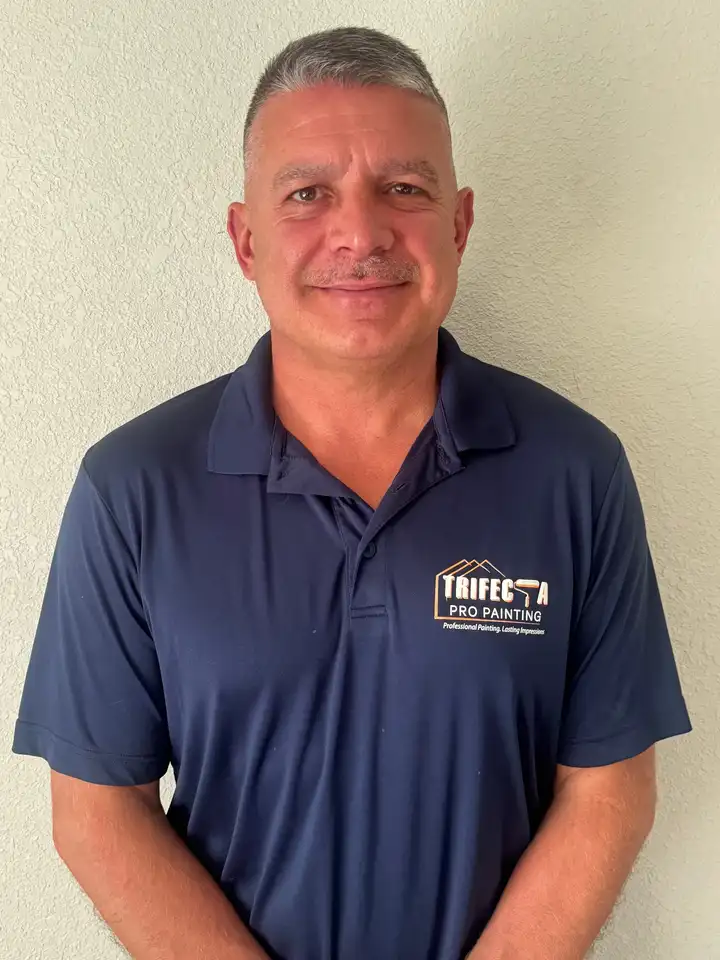 The owner of Trifecta Pro Painting in a navy company polo, standing against a light textured wall