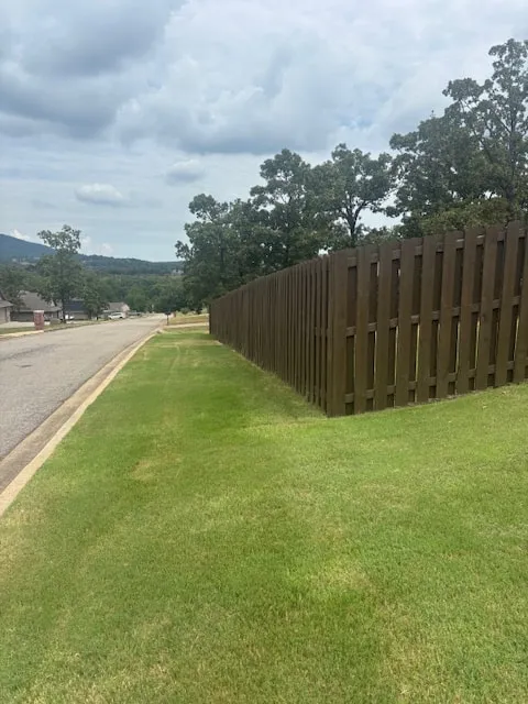 Dark stained wood fence running along a neighborhood street with a green lawn in front