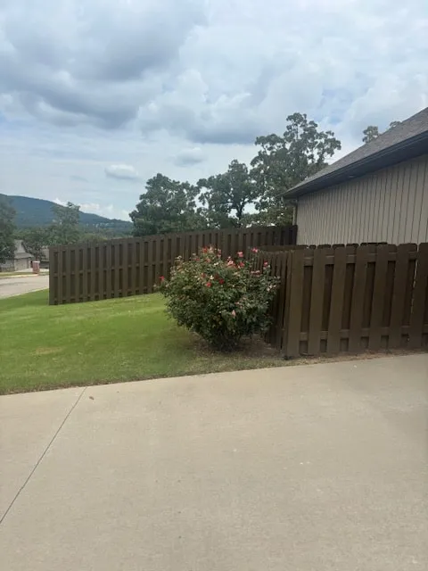 Dark stained fence along a concrete driveway with a rose bush in bloom and hills in the distance