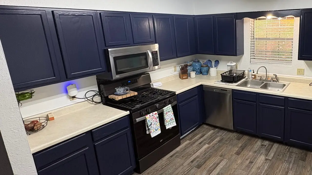 A kitchen after painting: Naval Blue cabinets above and below cream counters, a black range, a stainless refrigerator and a wood plank floor