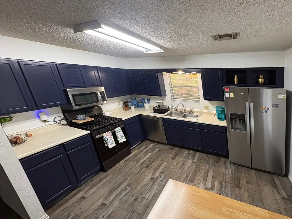 A kitchen after painting: Naval Blue cabinets above and below cream counters, a black range, a stainless refrigerator and a wood plank floor
