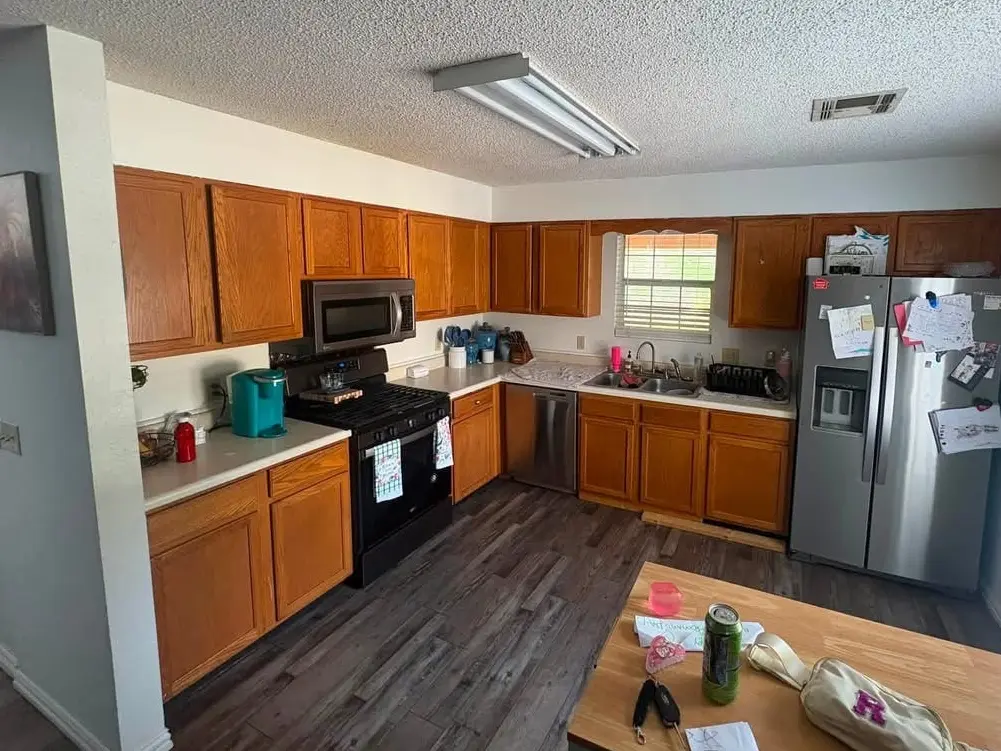 The same kitchen before painting: oak cabinets around a black range and a stainless microwave